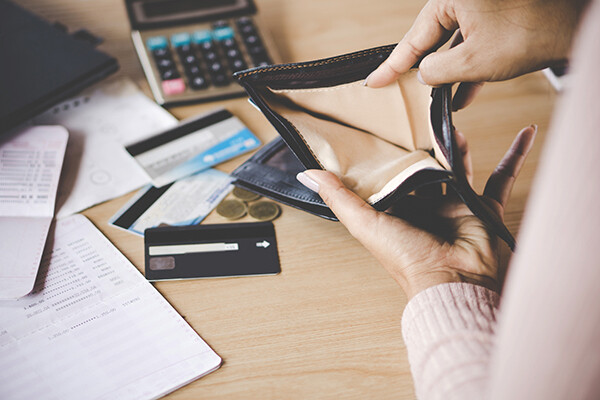 Closeup of a hand holding an empty wallet over a desk strewn with bank statements, credit cards and a calculator.