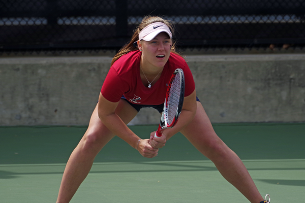 Bent at the knees, Iuliia Bryzgalova holds her tennis racquet with both hands and prepares to receive a serve.
