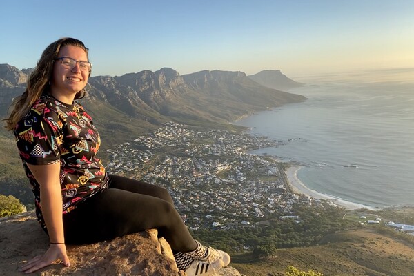 Smiling person sites on high ledge overlooking a coastal city