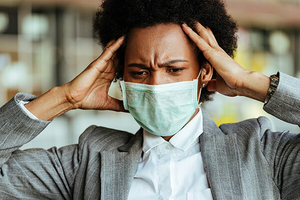 person holding their head feeling overwhelmed while wearing a face mask.