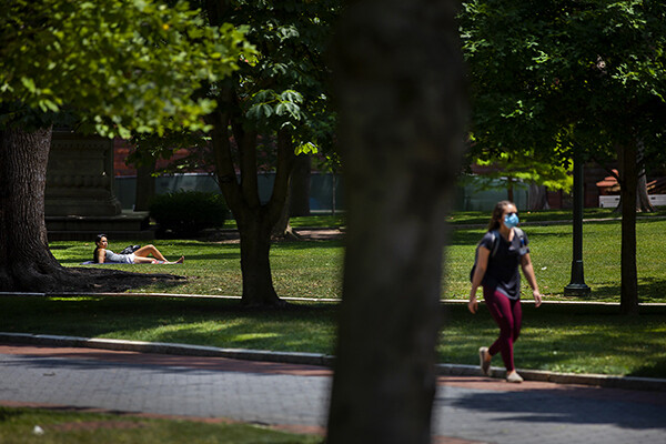 Person walking in sunshine along Locust Walk wearing a face mask.