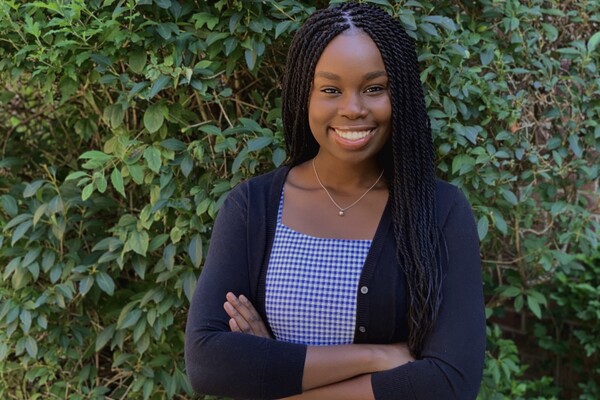 Student standing with arms crossed in front of foliage. 