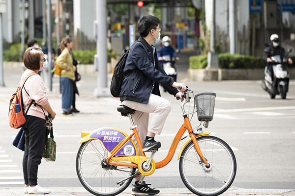 Pedestrians and bicyclists at a crosswalk wearing face coverings in a Taiwanese city.