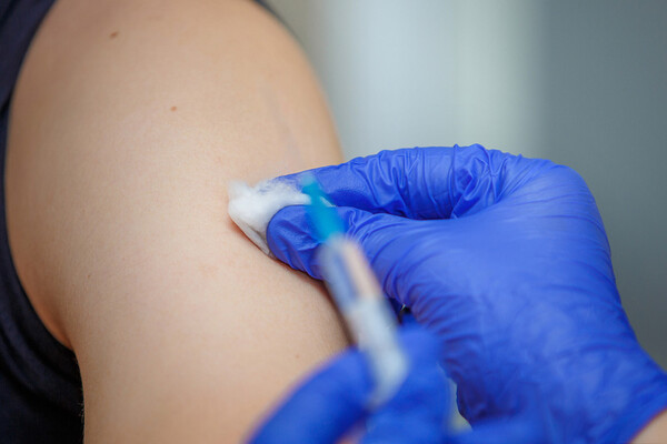 one gloved hand holds syringe and another cleans arm with cotton ball prior to vaccine