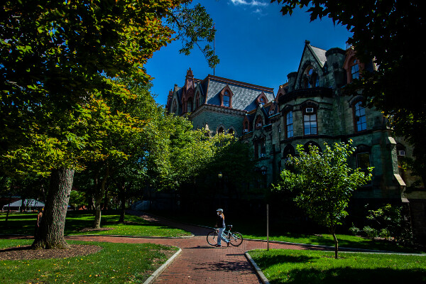 a person with a bike walking in front of college hall on a sunny day