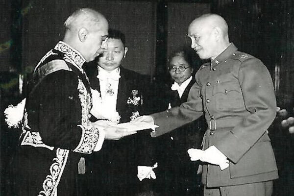 Two men shake hands and two others look on behind them in a black and white photo from the 1940s