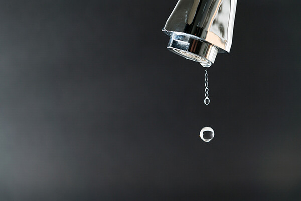 Tap faucet head with several drips of water dripping off the top.