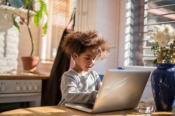 Young child on a laptop at the kitchen table.