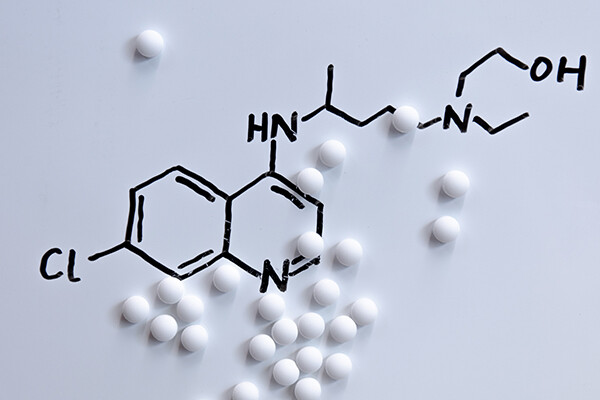 white pills on a surface with the molecular composition of hydroxychloroquine drawn.