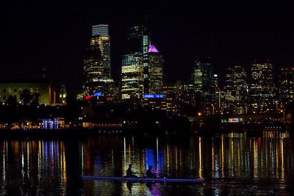 two people in a boat traveling past the philadelphia skyline at night