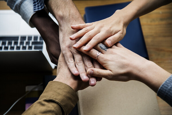 Five hands come together in a group; laptop in background