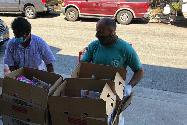 Two people wearing face coverings unload boxes of food for a food bank.