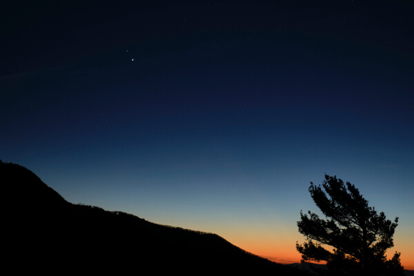 jupiter and saturn visible at dusk just above the horizon of a dark mountain landscape