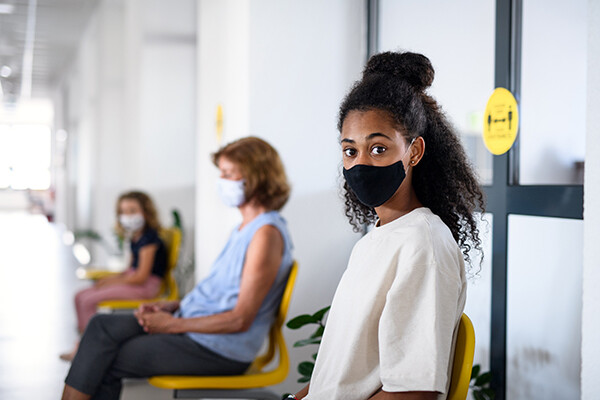 Teenager sitting in waiting room of a clinic wearing a face mask.