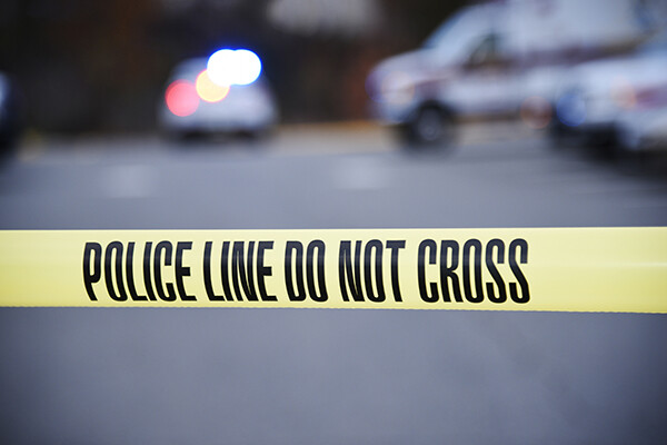 Police tape across a street with a police car and ambulance in background.