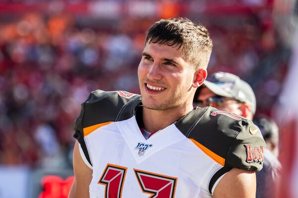 Justin Watson of the Tampa Bay Buccaneers stands on the sideline with his helmet off wearing his white jersey.
