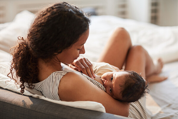African American woman breastfeeding a newborn baby on a couch.