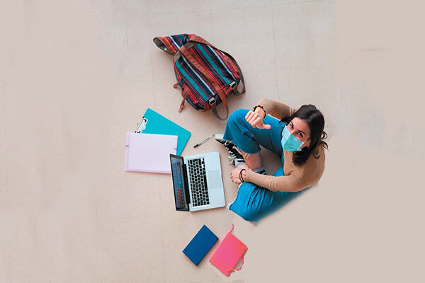 A masked student looks up while working on a laptop
