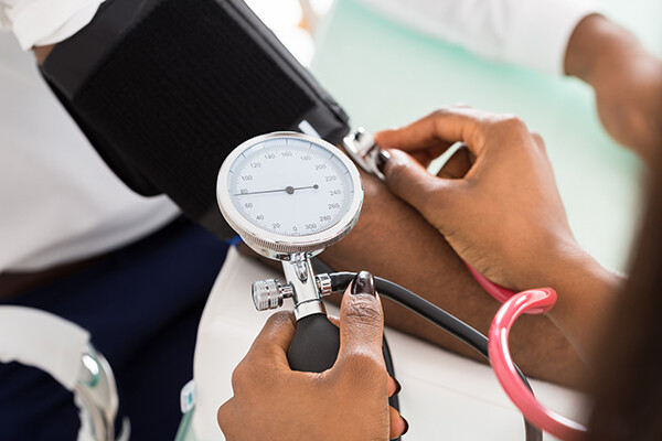 Hand holding a blood pressure gauge measuring the blood pressure of another person whose arm is extended.