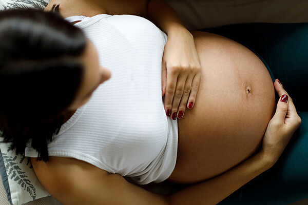 African American pregnant person laying back on a couch with pregnant belly exposed.