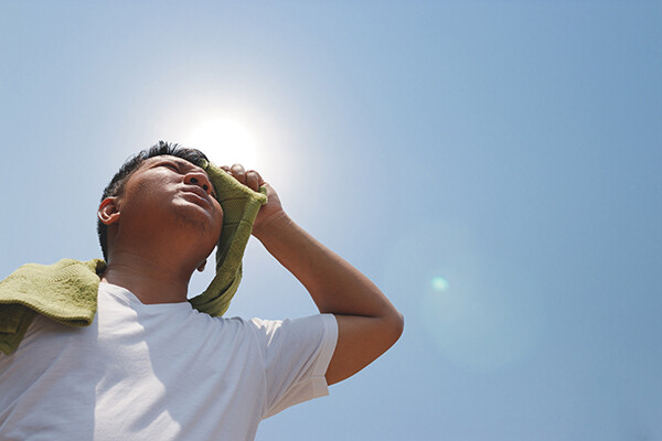 Person wiping sweat from their brow with a towel under the sun.
