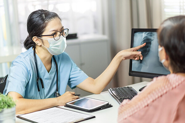 Doctor wearing a face mask sits at a desk looking at an x-ray with a masked patient.