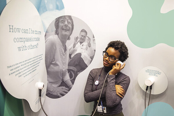 Person from Penn Medicine standing at one of the Listening Lab stations holding a headphone to their ear.