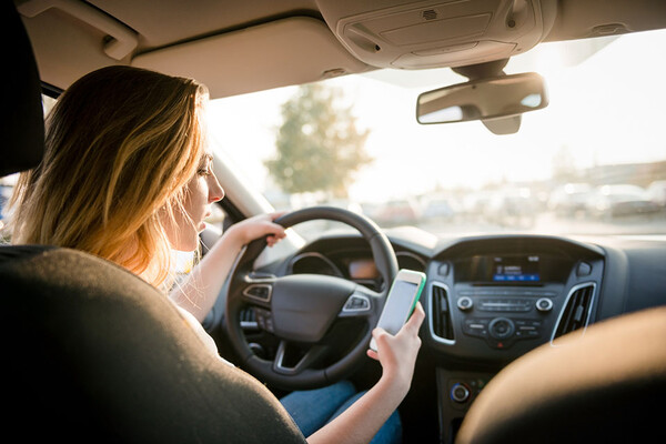 Adolescent in the driver’s seat of a car looking at their cell phone.
