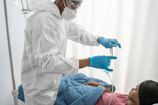 Black hospital patient in bed with nurse in full PPE preparing to put oxygen mask on patient’s face.