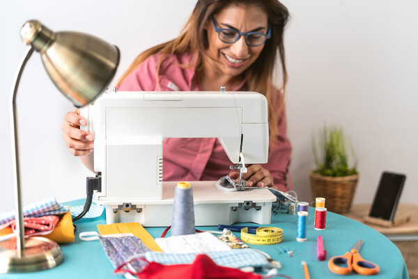 Person smiling at a sewing machine while making masks for COVID-19 face coverings.