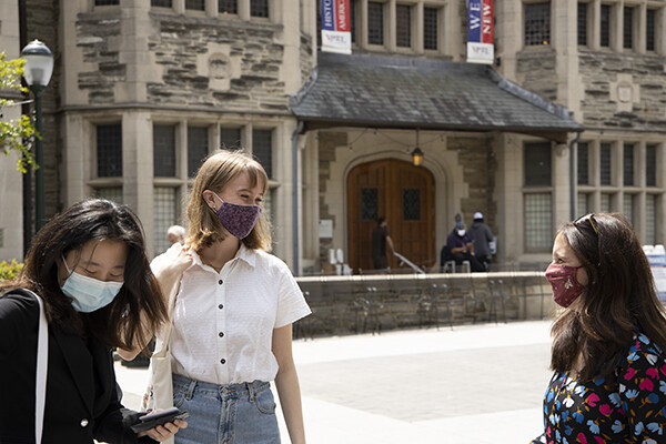 three women wearing mask smiles at each other in front of an old stone building