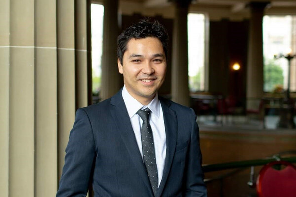 Damian Pang standing, smiling, in a suit.