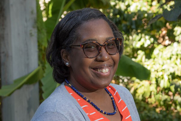 Person in glasses miles at the camera with green trees behind 