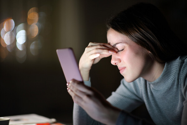 Person holding a smartphone close to their face rubs eyes.