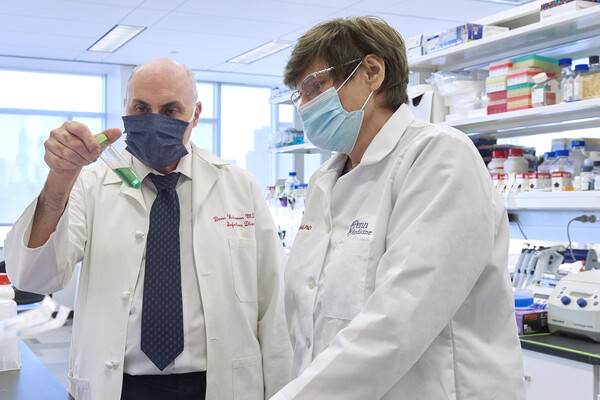 Drew Weisman and Katalin Kariko wear masks in a lab and look at liquid in a test tube.