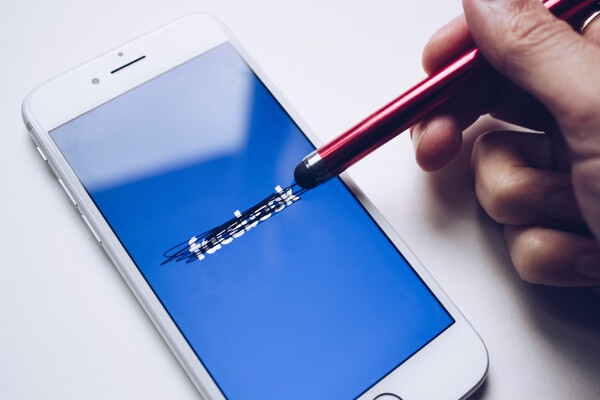 A white iphone bears a blue screen with the word "facebook" crossed out with a stylus