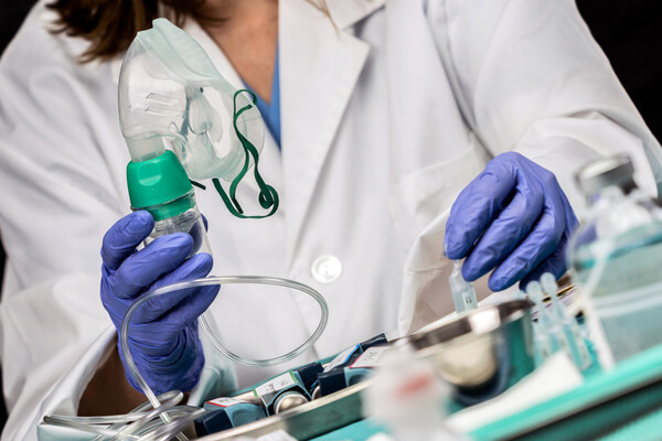 Doctor wearing a white coat and latex gloves holds up an oxygen mask.