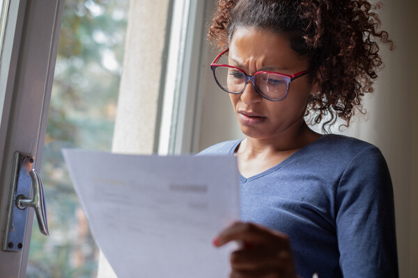 Concerned person standing by a window looking at a sheet of paper.