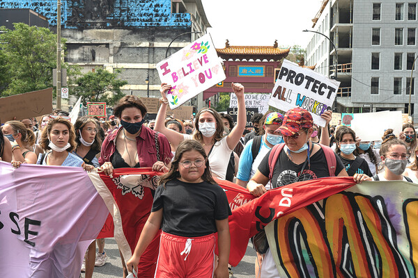 Masked people marching in protest holding signs that read I BELIEVE YOU and PROTECT ALL WORKERS.