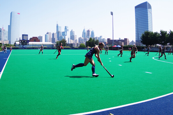 In the foreground, a Penn player dribbles the ball toward the goal with her stick during a home game at Vagelos Field.