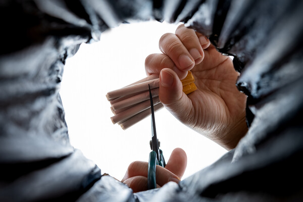 Hand holding scissors cutting a bunch of cigarettes in another hand held over a trash bin.