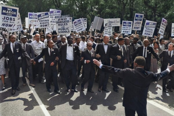 People march waving signs that say "end segregated rules in public schools" and "we demand voting rights now"