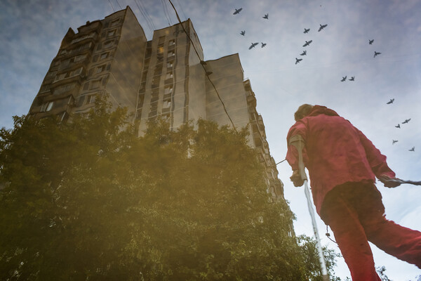 Person walking with cane past a tall apartment building.