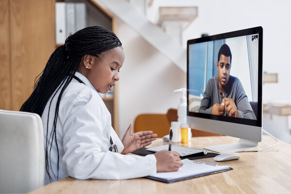 A patient having a telemedicine appointment with a doctor via a desktop computer screen.