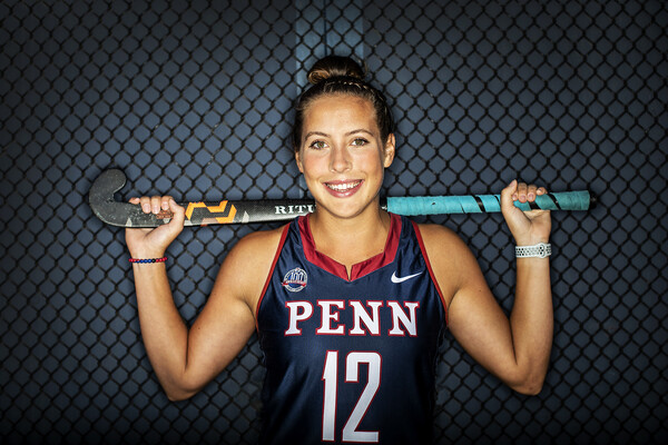 Gracyn Banks wears her field hockey jersey in front of net with her stick across her shoulders.