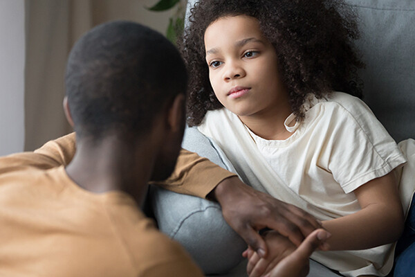 A concerned young child sitting on a couch listening to an adult.