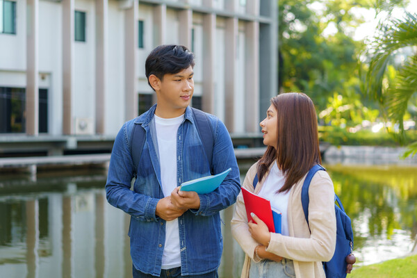 Two friends walking outside with backpacks and books.