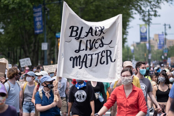 Group of protesters in masks in the streets, one carries a large sign that reads BLACK LIVES MATTER.