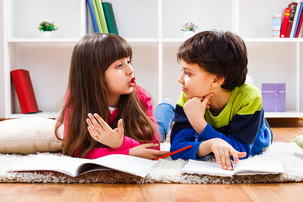 Two children lying on the floor talking over notebooks.