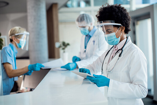 Three medical personnel in face masks and shields reviewing paperworks.